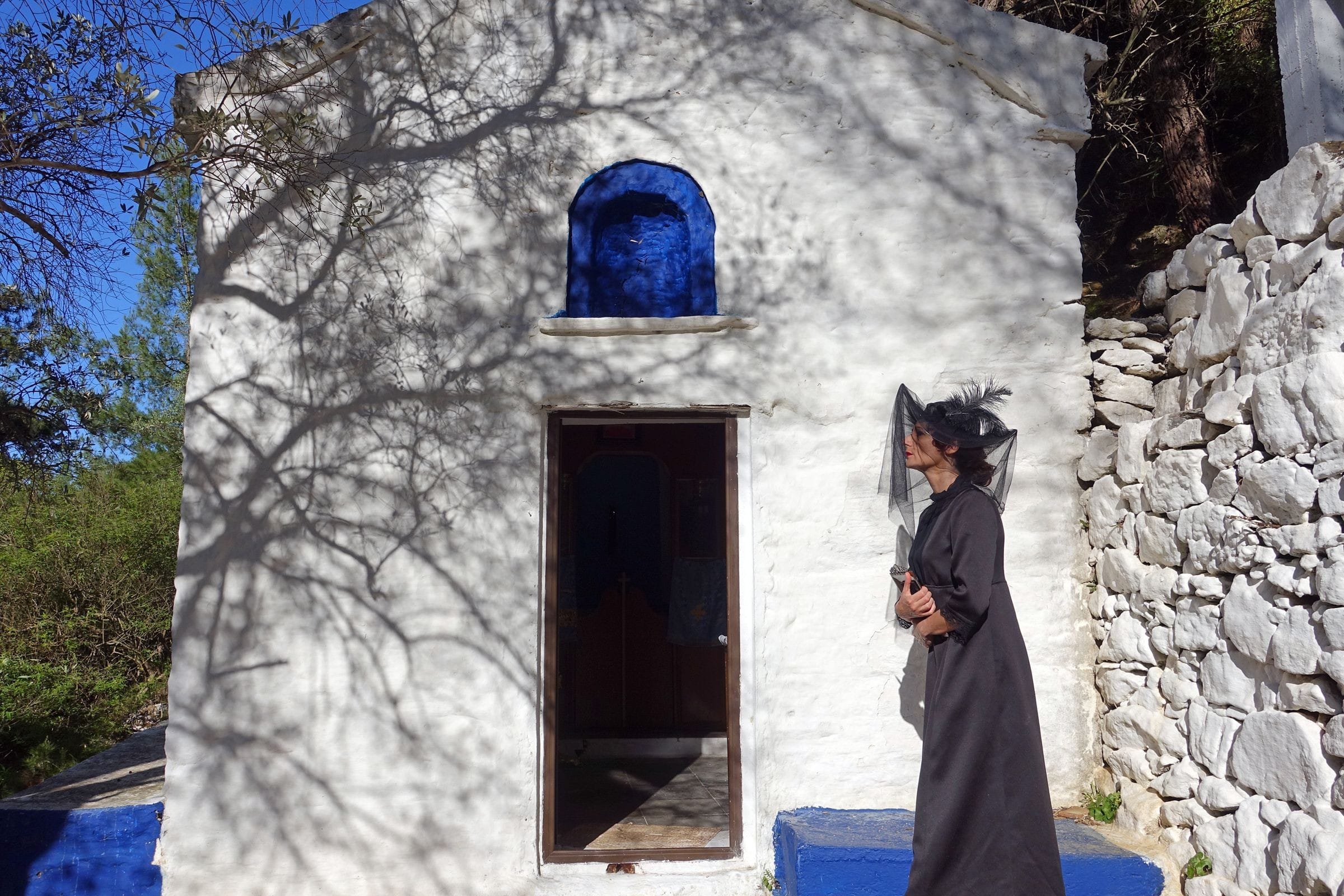 Portrait of woman outside small greek church with tree shadow.