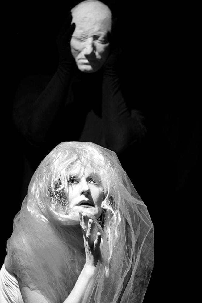Theatrical portrait of woman with haunting ghost like mask above her.